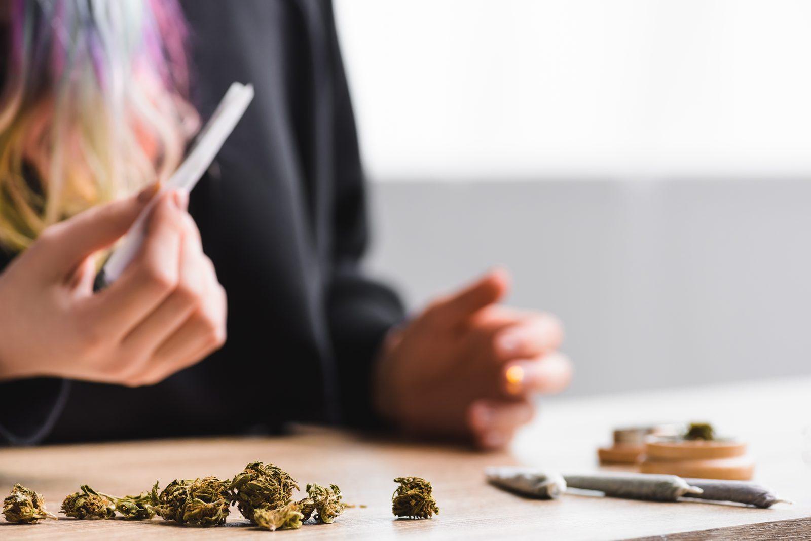 Hands rolling cigarette with herb on wooden table